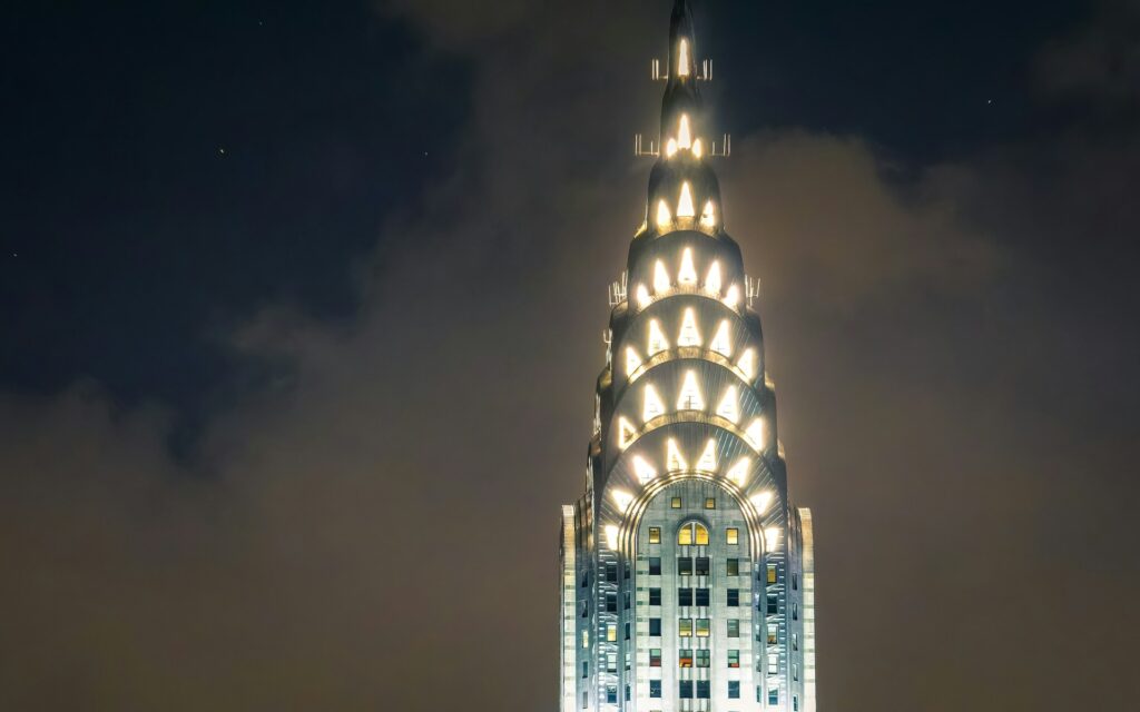 The peak of the Chrysler building, lit up at night in intricate patterns.