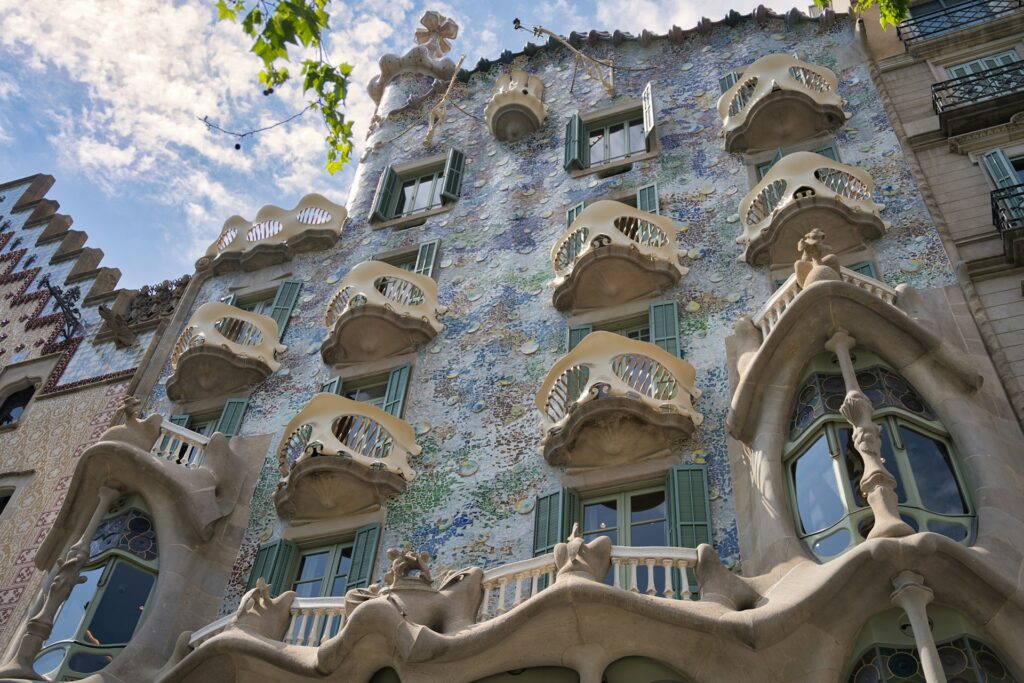 The front entrance of Casa BatllĂł, Barcelona. A bright exterior, with bone-like fences and curved windows.