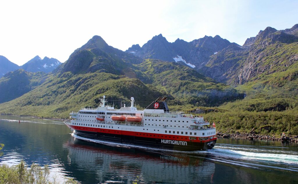 A Norwegian cruise ship sailing past mountainous fjords